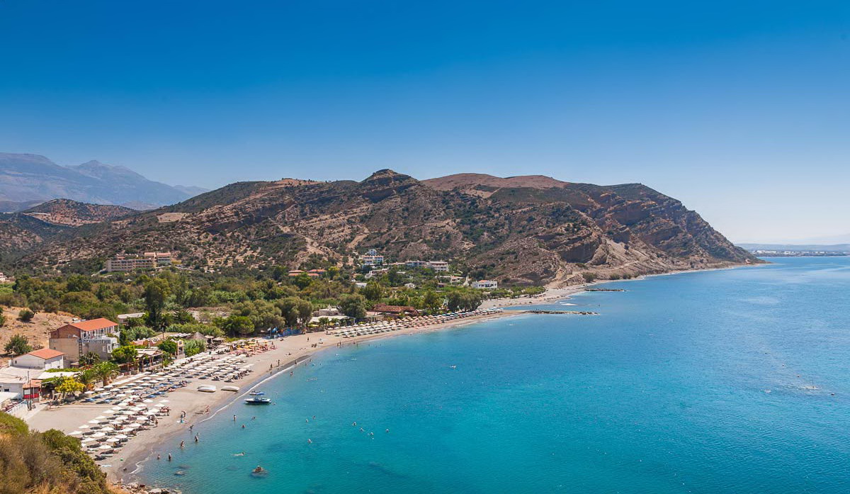 Long sandy beach of Agia Galini with crystal waters and mountain backdrop