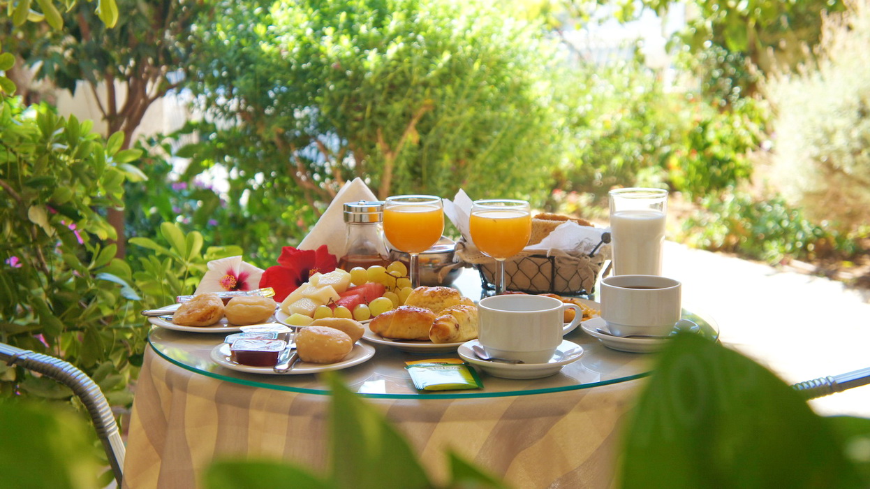 Breakfast table with fresh juice and pastries surrounded by greenery at IDI Hotel